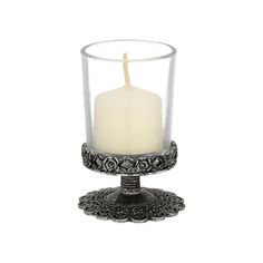 a white candle sitting in a glass on top of a metal stand with an ornate design