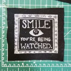 a black and white patch with the words smile you're being watched on it