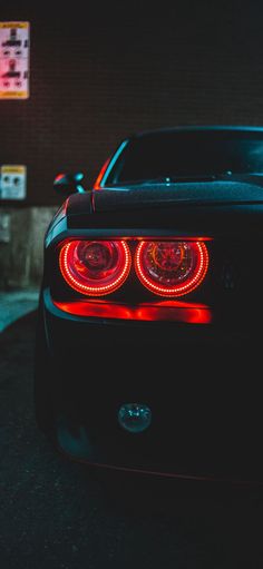 the rear end of a black sports car with its lights turned on at night time