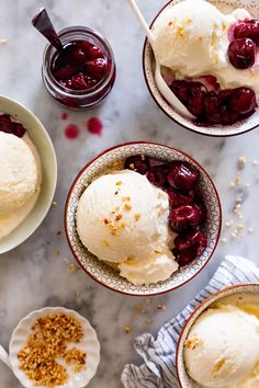 three bowls filled with ice cream and cherries on top of a marble countertop