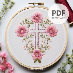 the cross is surrounded by pink flowers and green leaves, along with a spool of thread