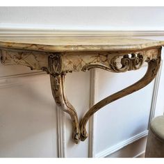 an ornate console table with marble top and carved wood carvings on the base, against a white painted wall