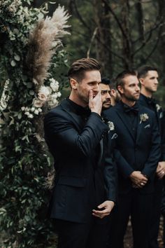 a group of men standing next to each other in front of a lush green forest