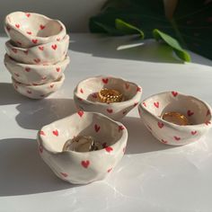 four bowls with hearts painted on them and gold rings in the middle one bowl is filled with coins