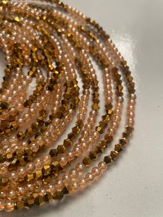 Elastic Waist Bead "Koun-Fao" crafted with resplendent gold glass crystal seed beads and adorned with delicate light brown glass seed bead accents. This elastic waist bead not only emanates opulence but also embodies a warm and earthy elegance, offering a comfortable and adjustable fit that transcends beauty and symbolism. 🌟 Gold Glass Crystal Seed Beads - Opulent Radiance: Koun-Fao is adorned with a luxurious array of gold glass crystal seed beads, creating an opulent radiance that symbolizes Brown Gold Beads Jewelry For Party, Spiritual Gold Multi-strand Beaded Bracelets, Bohemian Gold Beaded Bracelets With Spacer Beads, Gold Beaded Bracelets With Tiny Beads For Party, Bohemian Beaded Waist Beads For Parties, Gold Multi-strand Spiritual Beaded Bracelets, Gold Bohemian Beaded Bracelets For Festive Occasions, Gold Rondelle Beaded Bracelets With Colorful Beads, Gold Rondelle Beaded Bracelets With Tiny Beads