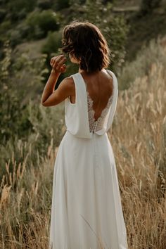 a woman in a white dress is standing in tall grass and looking at the sky