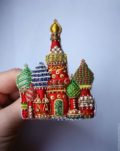 a hand holding a small red and green brooch with buildings on it's sides