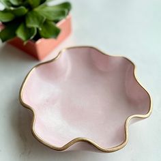 a pink and gold plate next to a potted plant on a white countertop