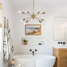 a white bath tub sitting next to a bathroom sink under a framed painting on the wall