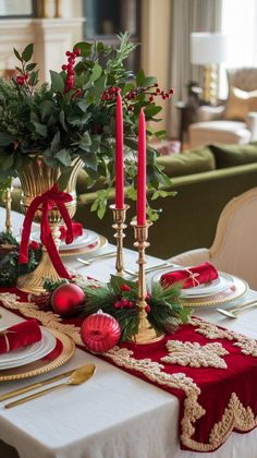 the table is set for christmas dinner with red and gold decorations, holly wreaths, candlesticks, and baubles