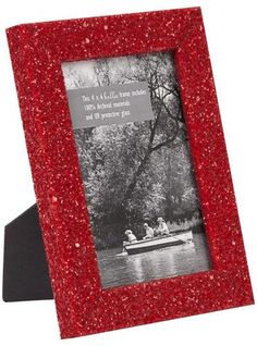 a red glittered photo frame with people in a boat on the water and trees behind it