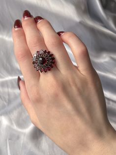 This angular double Bohemian garnet halo ring is just divine! Circa 1970, this piece pulls most of it’s design from the wildly popular bohemian garnet pieces of the 19th century Victorian era; which clustered these bright lustrous garnets together to hi-light their rich color. The double halo of garnets encircle a large central garnet in an almost sunflower-like formation due to the pointed cut of outermost halo, encompassing the flower child era it was created and paying homage to the bohemian garnet jewelry that came before it. A ring perfect for someone who loves statements with subtle hints of color, as the garnets are rather understated until they burst into a bright and brilliant cardinal red in direct light. Materials and Features: Garnet, 9ct Yellow Gold Age/Origin: Vintage, c 1970 Ruby Ring With Rose Cut Diamonds, Vintage Red Garnet Cluster Ring, Vintage Garnet Cluster Ring As Gift, Garnet Ring With 17 Jewels, Victorian Garnet Gemstone Rings, Elegant Red Garnet Cluster Ring, Vintage Garnet Cluster Ring With Gemstone, Victorian Ruby Cluster Ring With Gemstones, Elegant Multi-stone Garnet Rings