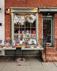 a table with many books on it in front of a brick storefront and door