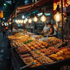 an outdoor food stand with many different foods on it's trays and lights hanging from the ceiling