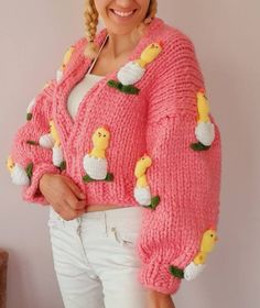 a woman wearing a pink sweater with yellow ducks on the front and white pants, smiling at the camera