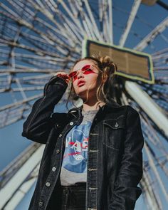 a woman wearing red sunglasses standing in front of a ferris wheel and talking on her cell phone