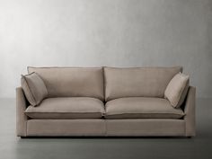 a couch with two pillows on top of it in front of a gray wall and floor