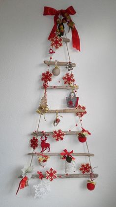 a christmas tree made out of wooden sticks and other ornaments hanging on the wall with red ribbon