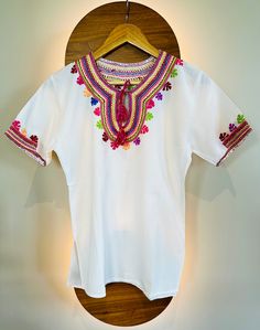 Introducing our exquisite Vintage Mexican Huipil blouse, a vibrant testament to the rich cultural heritage and artisanal mastery of Puebla, Mexico. Handcrafted with meticulous care by skilled artisans from indigenous communities, each Huipil is a unique embodiment of traditional craftsmanship and contemporary flair. Adorned with multicolored embroidery, every stitch tells a story, weaving together centuries of Mexican artistry into a breathtaking tapestry of color and design. Sourced directly from artisan communities, this Huipil captures the essence of Mexican tradition while celebrating the ingenuity of local designers. Designed to embrace the body in relaxed elegance, our Huipil boasts a loose-fitting silhouette that effortlessly flatters Small to Large sizes, ensuring a comfortable and Indigenous Mexican Clothing, Festive White Tops With Motifs, Festive White Top With Motifs, Bohemian Tops With Floral Embroidery For Navratri, Traditional Blouse For Navratri Rituals, Traditional White Embroidered Top, Bohemian Multicolor Embroidered Tops For Navratri, Bohemian Tops With Multicolor Embroidery For Navratri, Festive Multicolor Bohemian Tops