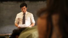 a man standing in front of a blackboard while wearing a tie and holding papers