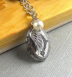 "This Vintage inspired necklace is 28\" long. Small oval silver finished locket with Victorian patterns engraved on the sides is decorated with antique finished tiny silver wing and white swarovski pearl. Pendant locket is finished with silver chain and silver lobster clasp. Locket is almost 23mm in size and opens side ways. It has room for two photos! Thanks for looking:) ~Mani" Antique Silver Locket Necklace With Oval Pendant, Antique Silver Oval Pendant Locket Necklace, Antique Silver Oval Pendant Necklace With Locket, Antique Silver Necklace With Oval Locket Pendant, Silver Vintage Charm Oval Pendant Jewelry, Antique Silver Necklaces With Oval Vintage Charm, Antique Silver Necklace With Vintage Charm, Antique Silver Necklace With Vintage Charm In Oval Shape, Antique Silver Oval Necklace With Vintage Charm