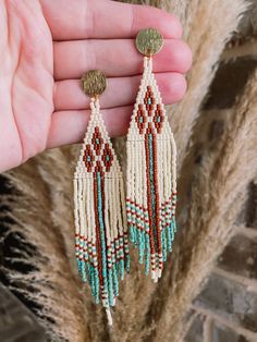 a pair of earrings is being held in front of a brick wall and dried grass