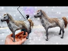 a hand is holding two miniature horses in the snow