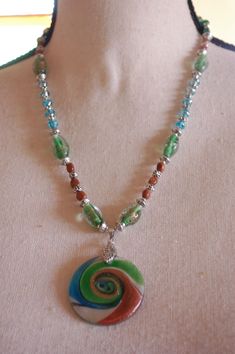 I designed and hand crafted this lovely hand beaded pendant necklace.  It has a beautiful lampworked glass pendant, and lampworked glass, natural stone, glass, and silver metallic beads.    The lampworked glass pendant and beads have a bit of sparkle - for just a touch of bling!  The colors are green, turquoise, bronze, silver, and clear/white.   This unique necklace measures 21 inches in length, and the pendant adds an additional 2.25 Inches.  It has a J-hook clasp, and is comfortable to wear. Ours is a non-smoking home. Beaded Czech Glass Pendant Necklace, Artistic Glass Necklace With Round Pendant, Artistic Glass Round Pendant Necklaces, Handmade Czech Glass Necklace With Round Pendant, Handmade Czech Glass Round Pendant Necklace, Artistic Round Glass Necklaces, Artistic Glass Round Pendant Necklace, Green Beaded Jewelry From Recycled Glass, Czech Glass Round Pendant Necklaces As Gifts