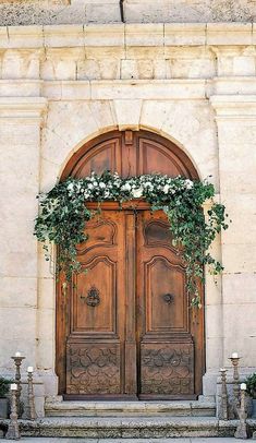 an old wooden door with flowers growing on the top and bottom, in front of a stone building