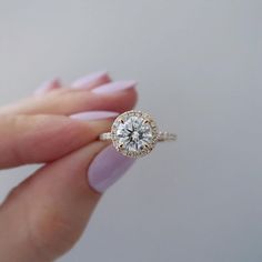 a woman's hand holding an engagement ring with a diamond center and halo setting