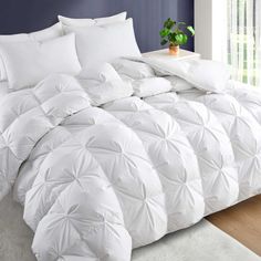 the comforter is white in color and has many pillows on it, as well as a potted plant