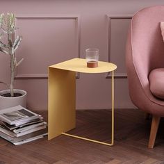 a small yellow table next to a pink chair and a potted plant on the floor