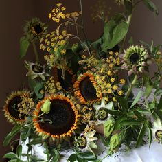 an arrangement of sunflowers and other flowers on a tablecloth with green leaves