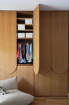 an open closet with clothes hanging on the door and drawers in it, next to a bed