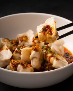 a white bowl filled with dumplings covered in sauce and topped with chopsticks