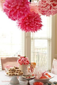 a table topped with lots of desserts and paper pom poms hanging from the ceiling