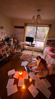 a woman sitting on the floor in front of a laptop computer surrounded by papers and candles