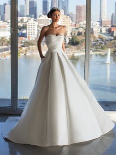 a woman standing in front of a window wearing a wedding dress