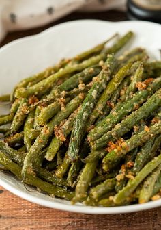 a white bowl filled with green beans covered in seasoning on top of a wooden table