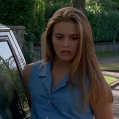 a woman standing next to a car with her hand on the door and looking angry