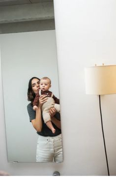 a woman holding a baby in front of a mirror