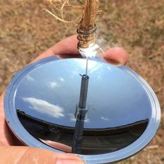 a person holding a small round object in their hand, with the reflection of clouds on it