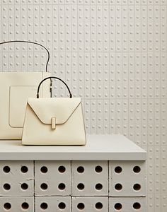 two white purses sitting on top of a table next to each other with holes in the wall behind them