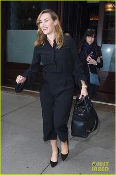 a woman in black is walking down the street with her hand on her hip bag