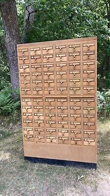 an old wooden mailbox with many drawers in the grass next to some trees and bushes