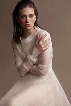 a woman in a white dress is posing for a photo with her hands on her chest