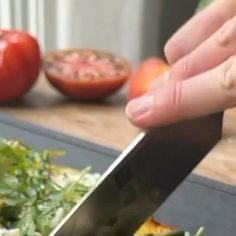 a person is cutting up some food with a knife on a table next to tomatoes and lettuce