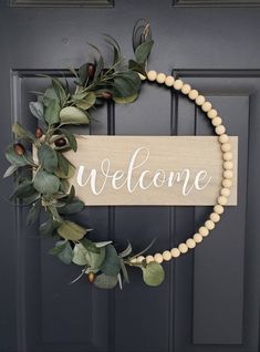 a welcome sign hanging on the front door with greenery and beads around it's edges