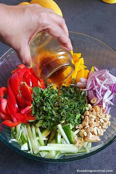 someone pouring dressing into a glass bowl filled with chopped vegetables and other foodstuffs