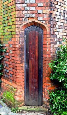 an old red brick building with a wooden door and window in the center surrounded by greenery